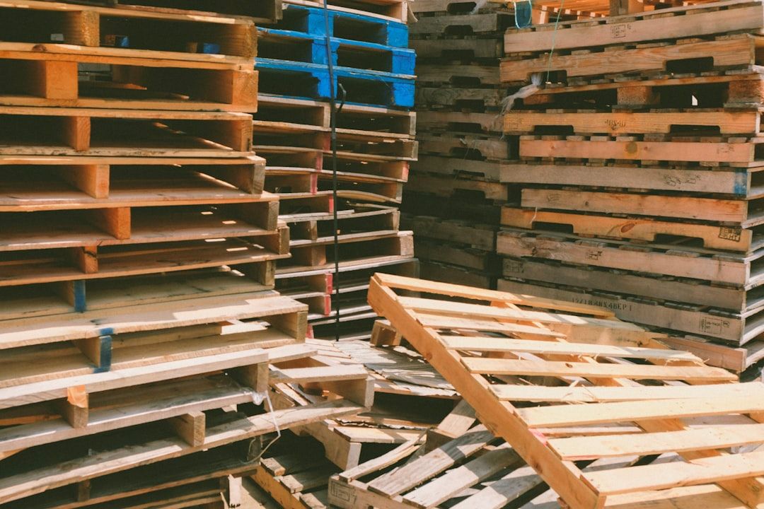 Gestapelde houten pallets in zonlicht, waarvan sommige blauw zijn geverfd.