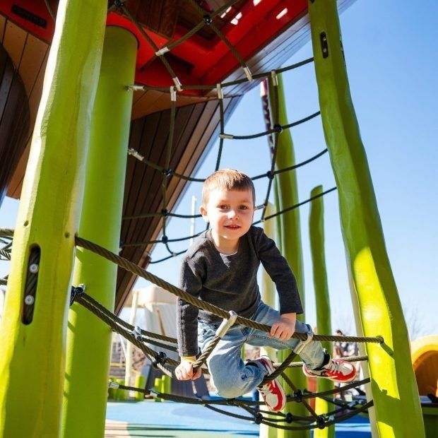 Jongen beweegt over een klimnet op een kleurrijke buitenspeelplaats
